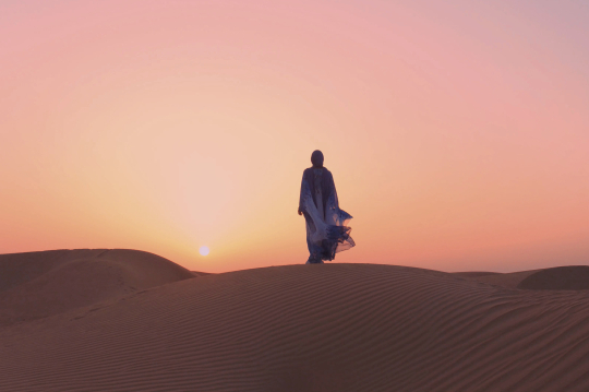 Frau im Gewand auf einer Sanddüne im Sonnenuntergang